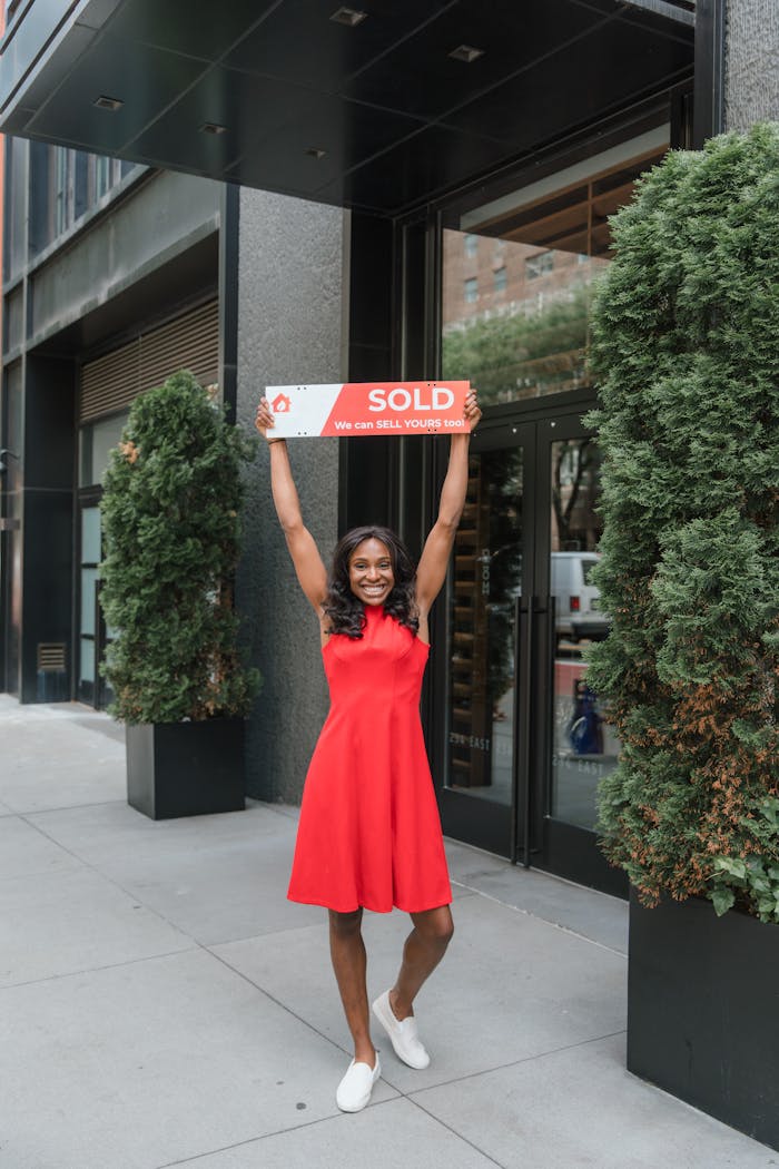 The Art of Drawing Readers In: Your attractive post title goes here Smiling woman in red dress celebrating real estate sale with a sold sign outdoors.